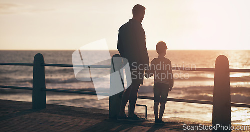 Image of Silhouette, sunset and a father holding hands with his son on the promenade at the beach while walking together. View, family or kids and a man bonding with his young male child outdoor in nature