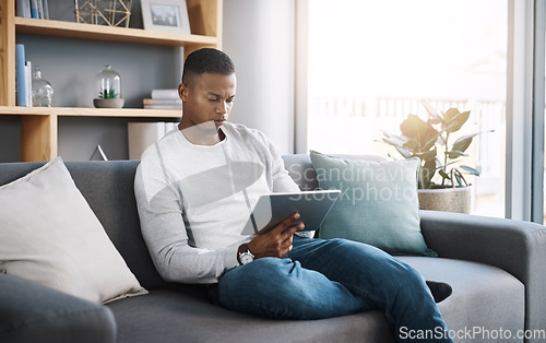 Image of Remote work, tablet and man on sofa reading email, social media post or streaming video on subscription service. Search, scroll and internet, freelance worker checking website on couch in living room