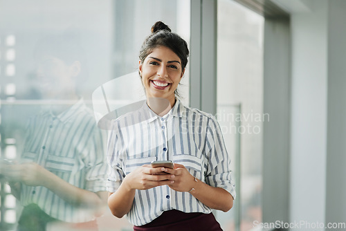 Image of Business woman, portrait and phone with happiness at office window with a smile. Young female face employee and mobile connection of a worker feeling happy on social media and technology at company