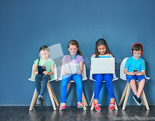 Image of Children with a laptop, tablet and phone for learning and education while online for research on internet. Kids or students against a blue mockup wall with technology on chairs in a waiting room