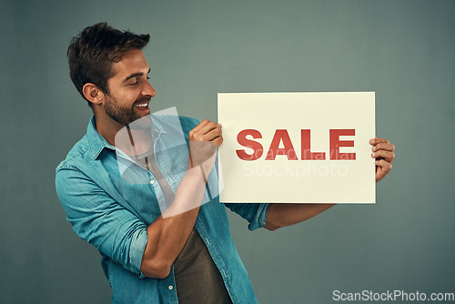 Image of Happy man, hands and sale sign for advertising, marketing or branding against a grey studio background. Male person or realtor holding board or poster with smile for sales or market advertisement