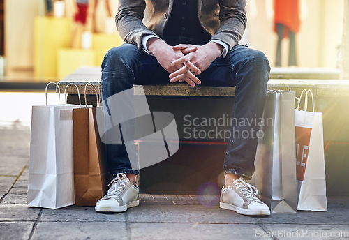 Image of City, man sitting and sale with shopping bags on floor, sidewalk or street with sneakers, relax or waiting for taxi. Guy, retail and fashion on bench in metro cbd with discount, promotion or clothes