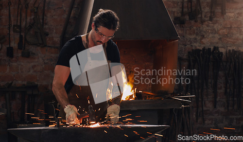 Image of Hammer, anvil and fire with a man working in a forge for metal work manufacturing or production. Industry, welding and trade with a male blacksmith at work in a factory, plant or industrial workshop