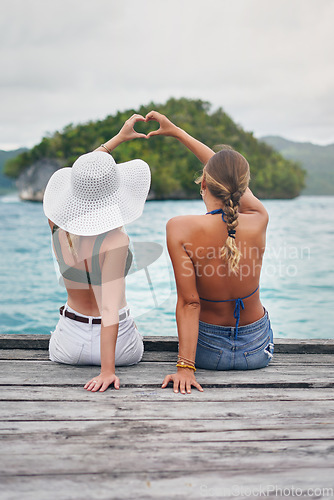 Image of Women, lake and friends outdoor with heart hand sign on deck to relax with peace, water and love. Back of female people with hands, icon and freedom on vacation, holiday or summer adventure in nature