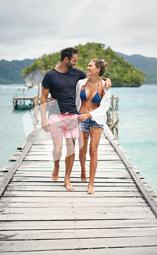 Image of Happy couple, tropical and ocean boardwalk with walking, hug and outdoor in summer sunshine for holiday. Man, woman and walk together by sea with love, happiness and care with travel for vacation