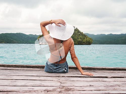 Image of Back, relax and woman at a river dock while on a tropical summer vacation or weekend trip. Travel, outdoor and female person with hat sitting on wood pier by lake water on a paradise holiday in Bali.