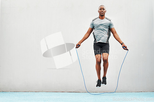 Image of Jump, rope and training with black man skipping in stadium for sports, workout practice and cardio. Health and body with athlete jumping on track for strong, mockup space and exercise against wall