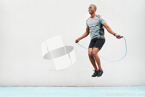 Image of Jump, rope and space with black man skipping in stadium for sports, workout and cardio. Performance, health and body with male athlete training on track for strong, mockup and exercise by wall