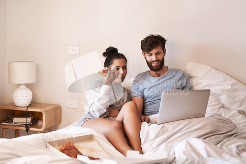 Image of Couple, pizza and movie on laptop in bed with junk food and streaming series. Eating, computer video and meal in a bedroom at home with man and woman together with bonding and online watching