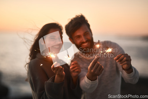 Image of Happy, beach and couple with sparklers for celebration and party with sparks on romantic date. Love, sunset and excited man and woman with fireworks for honeymoon on holiday, weekend and vacation