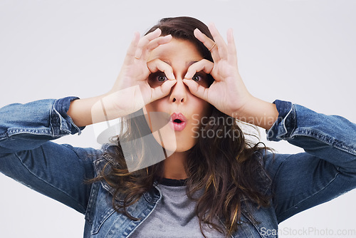 Image of Portrait, funny face and finger glasses with a woman in studio on a gray background looking silly or goofy. Comedy, comic and playing with a crazy young female person joking indoor for fun or humor