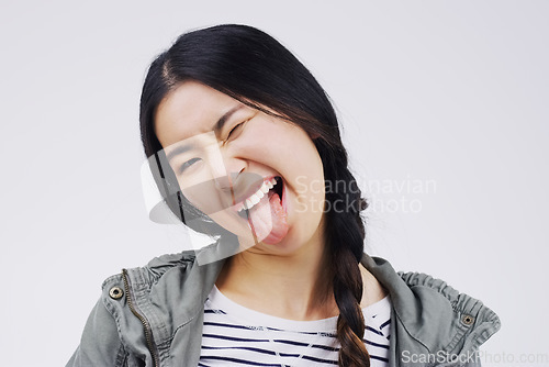 Image of Portrait, funny face and tongue with an asian woman in studio on a white background looking silly or goofy. Comedy, comic and wink with a crazy young female person joking indoor for fun or humor