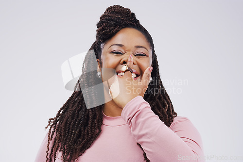 Image of Portrait, funny face and finger on nose with a black woman in studio on a gray background looking silly or goofy. Comedy, comic and nostril with a crazy young female person joking for fun or humor