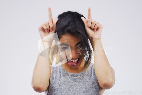 Image of Portrait, funny face and devil horns with a woman in studio on a gray background looking silly or goofy. Comedy, comic and playing with a crazy young female person joking for carefree fun or humor