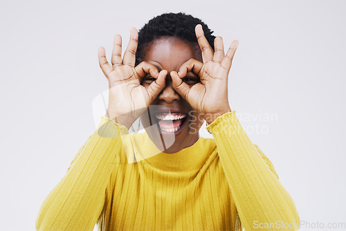 Image of Portrait, funny face and finger glasses with a black woman laughing in studio on a white background for humor. Comic, comedy and hands on eyes with a playful young female person joking or having fun