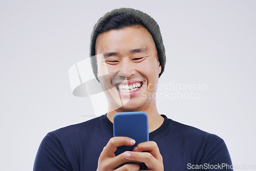 Image of Phone, laugh and Asian man online in studio with smile for social media, internet humor and funny chat. Communication, gray background and male person on smartphone for website, mobile app and meme
