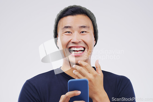 Image of Comic, portrait and Asian man with a smartphone, funny and happiness against a grey studio background. Face, male person and guy with a cellphone, mobile app and meme with a smile, joy and connection