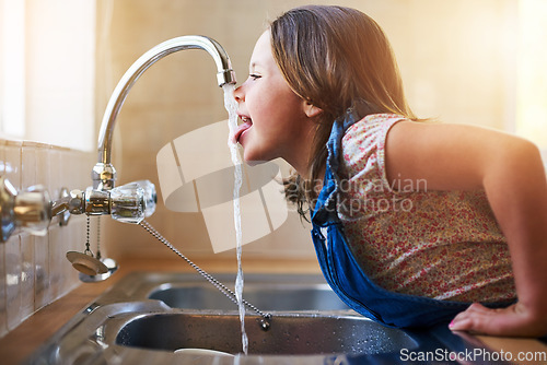 Image of Drinking water, tap and child with tongue out in a home kitchen with a smile. House, kids and youth feeling thirsty, cheeky and curious at a sink trying to drink from faucet for hydration alone