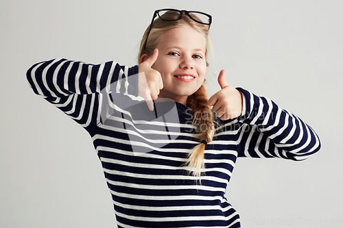 Image of Thank you, thumbs up and portrait of young girl or child doing yes, celebrate or happy sign with hand. Glasses, agree and female kid or person smile and like gesture in a grey studio background