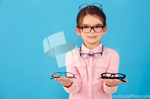 Image of Portrait, mockup and choice by kid with glasses for vision or eye care promotion isolated in a blue studio background. Smile, decision and girl child with sale, discount and deal option for eyewear