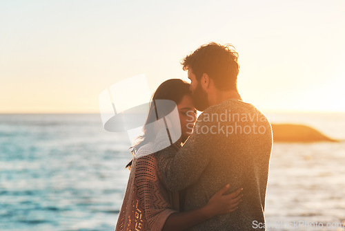 Image of Sunset, beach and couple kiss forehead for relax, bonding and quality time on romantic date. Nature, travel and man and woman embrace for anniversary or honeymoon on holiday, weekend and vacation