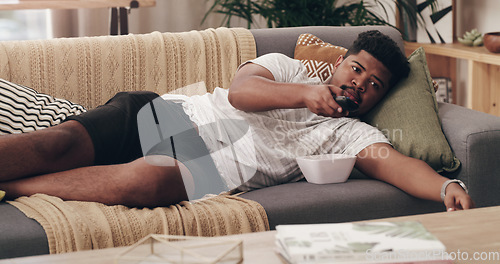 Image of Relax, lazy and a man watching tv on a sofa in the living room of his home over the weekend. Television, video and subscription streaming service to watch a movie in his house for entertainment