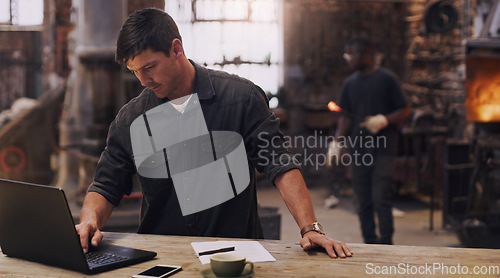 Image of Workshop, man and working on laptop in metal blacksmith factory for trade business, finance and industry technology. Welder, computer and online paperwork for businessman, staff and forge worker