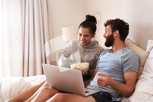 Image of Laptop, watching movie and popcorn with laughing couple in bed for streaming, relax or internet. Subscription, happy or comic man and woman at home for social media, funny and free time on weekend