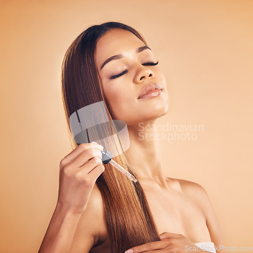 Image of Woman, hair care and studio with serum, oil or drop for wellness, health and growth by brown background. Young model, girl and product for healthy haircare, results and texture with glow by backdrop