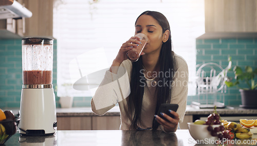 Image of Smoothie, phone and woman in kitchen for breakfast, texting and healthy diet in her home. Fruit, shake and female health influencer with smartphone app for social media, blog or vlog for vegan recipe
