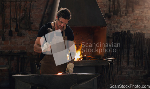 Image of Hammer, anvil and fire with a man working in a foundry for metal work manufacturing or production. Industry, welding and trade with a young male blacksmith in a workshop, plant or industrial forge