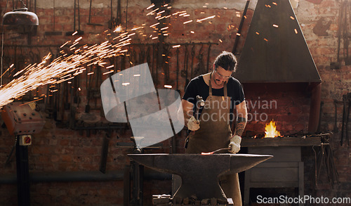 Image of Hammer, anvil and fire with a man working in a factory for metal work manufacturing or production. Industry, welding and trade with a male blacksmith at work in a forge, plant or industrial workshop