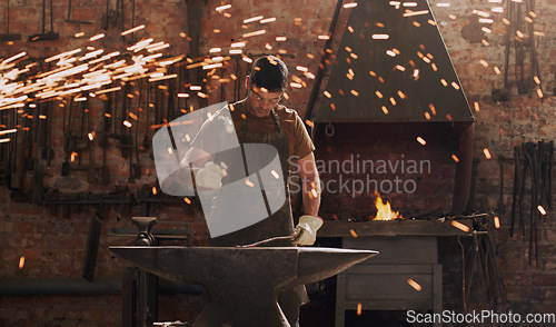 Image of Hammer, anvil and fire with a man in a forge workshop for metal work manufacturing or production. Industry, welding and trade with a male blacksmith at work in a factory, plant or industrial foundry