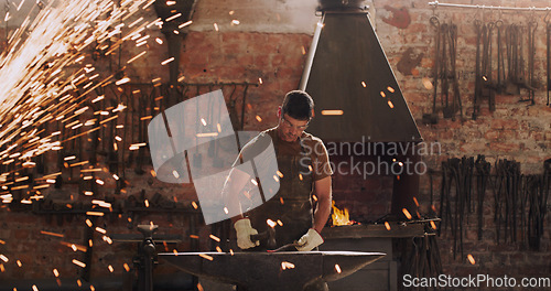 Image of Hammer, anvil and sparks with a man at work in a forge for metal work manufacturing or production. Industry, welding and trade with a male blacksmith working in a factory, plant or industrial foundry