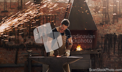 Image of Hammer, anvil and fire with a man working in a plant for metal work manufacturing or production. Industry, welding and trade with a male blacksmith at work in a factory, forge or industrial workshop