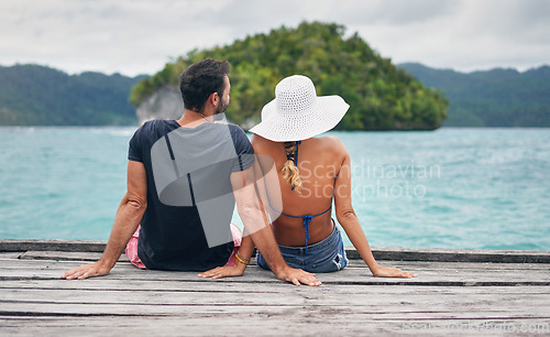 Image of Back, couple and vacation together on ocean deck, dock or sitting on boardwalk to relax or enjoy the sea or water landscape. People, man and woman on holiday, summer travel or date in tropical nature