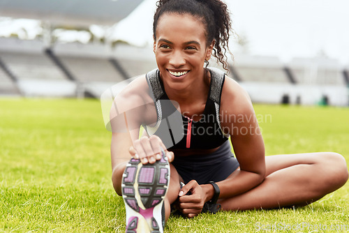 Image of Happy woman, smile and stretching legs on grass at stadium in preparation for running, exercise or workout. African female person smiling in warm up leg stretch for fitness, sports or run on a field
