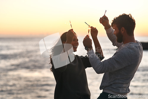 Image of Sunset, beach and couple with sparklers for celebration, party and quality time on romantic date. Nature, love and happy man and woman with fireworks for honeymoon on holiday, weekend and vacation
