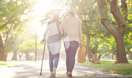 Image of Walking, park and and woman with elderly mother for bonding, assistance and help outdoors. Nature, family and female person with disability with cane and adult daughter for wellness, relax or support