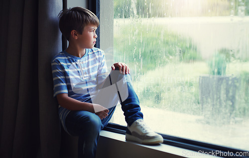 Image of Little boy, home and watching the rain by window of natural water drops and thinking in relax indoors. Child relaxing by windowsill looking out glass at storm in lonely or sad for weather at house