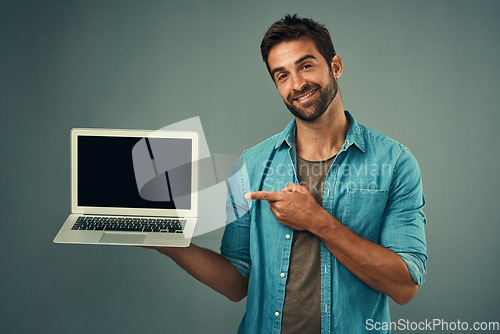 Image of Happy man, laptop and pointing to mockup screen for advertising or marketing against a grey studio background. Portrait of male person showing computer display or mock up space for advertisement