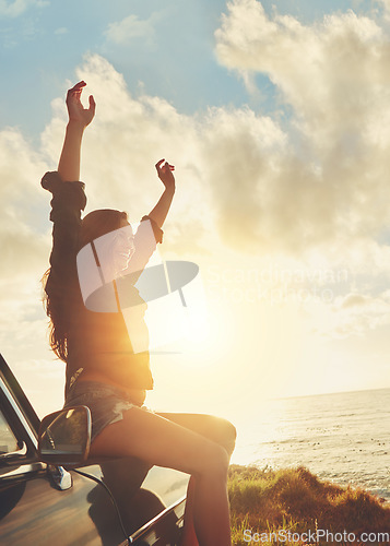 Image of Road trip, view and arms raised with a woman at the coast, sitting on her car bonnet during travel for freedom or escape. Nature, flare and water with a female tourist traveling in summer at sunset