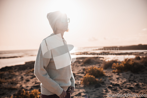 Image of Portrait of young stylish woman wearing wool sweater, wool cap and sunglasses on long sandy beach in spring