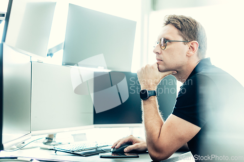 Image of Stock broker trading online watching charts and data analyses on multiple computer screens.