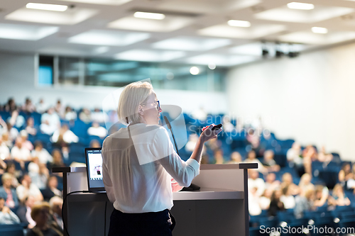 Image of Female speaker giving a talk on corporate business conference. Unrecognizable people in audience at conference hall. Business and Entrepreneurship event.