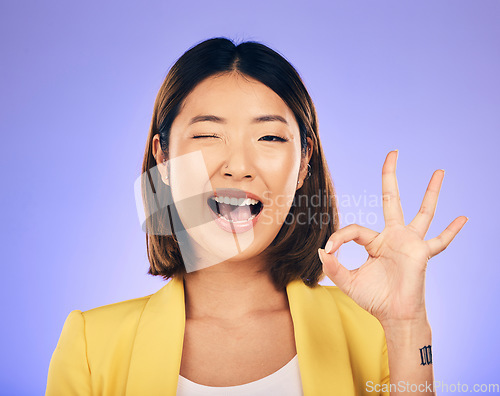 Image of Portrait, smile and Asian woman with ok sign, wink and emoji against a studio background. Face, female person and model with happiness, hand gesture and symbol for thank you, perfect and approval
