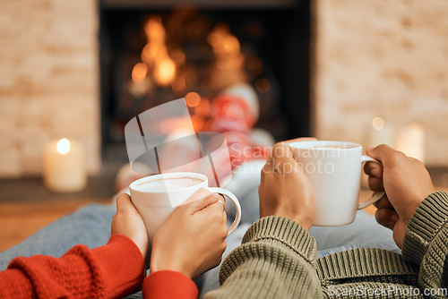 Image of Hands, coffee and couple relax by fireplace, bonding and cozy in home together. Tea, man and woman relaxing by fire on Christmas holiday in winter, heat and enjoying quality time with drinks in house