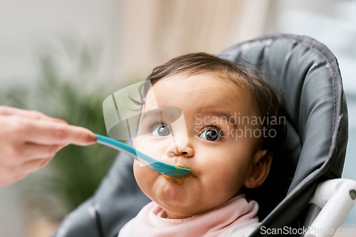 Image of Cute, sweet and girl baby eating puree for lunch, dinner or snack in her high chair at home. Child development, food and infant kid enjoying a meal with a spoon for growth and wellness in a house.