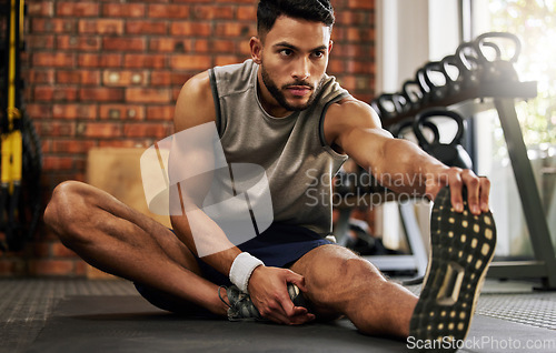 Image of Gym, man sitting and stretching legs for workout warm up, motivation and fitness mindset with hand on foot. Focus, commitment and male athlete on floor, leg stretch at sports club for exercise goals