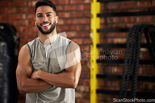 Image of Fitness, earphones and portrait of man in gym, arms crossed and confident smile in mockup space. Happiness, workout and happy face of bodybuilder streaming music for health, indoor training and pride